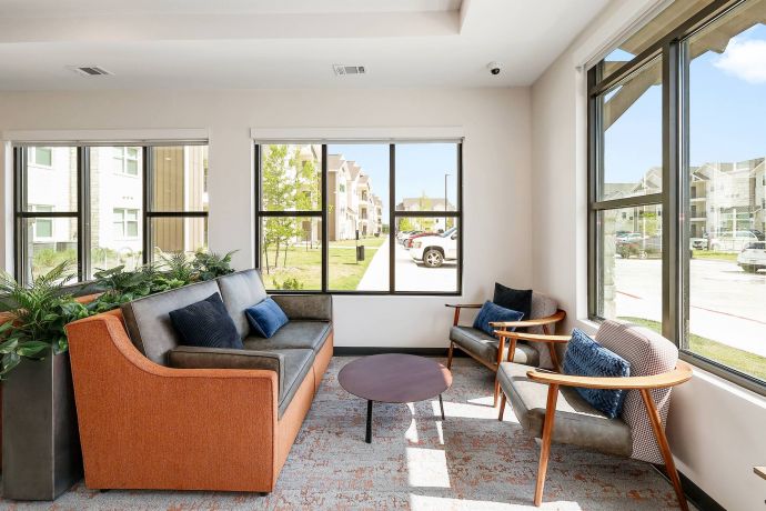 The Narrows Modern lounge area with a sofa, two chairs, a round table, and large windows letting in natural light.