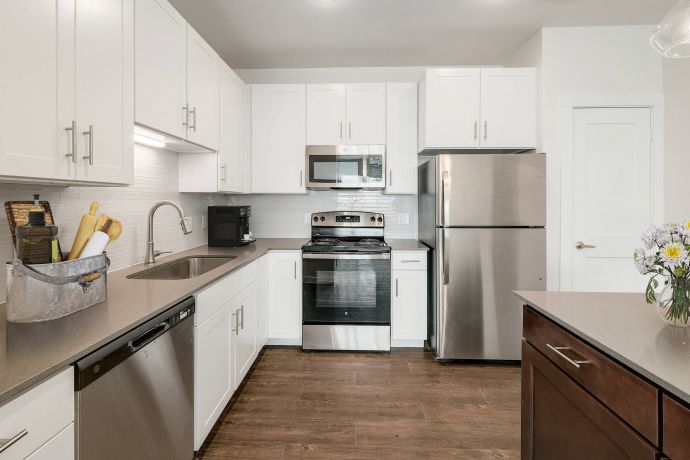 The Narrows Modern kitchen with white cabinets, stainless steel appliances, brown floors, and a vase of flowers on the counter.