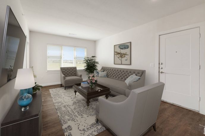 The Narrows Bright living room with gray sofas, a coffee table, rug, lamps, and wall art near a front door and windows.