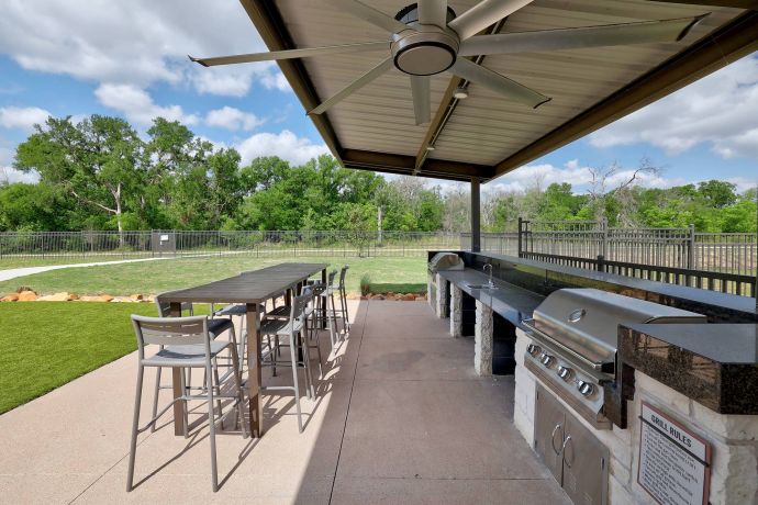 The Narrows Outdoor covered patio with a long dining table, chairs, and built-in grill stations overlooking a grassy area.