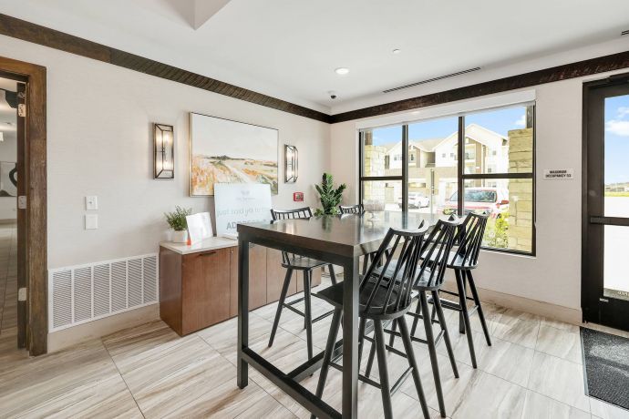 The Narrows Modern room with a tall black table, five chairs, wall art, plants, and large windows letting in natural light.