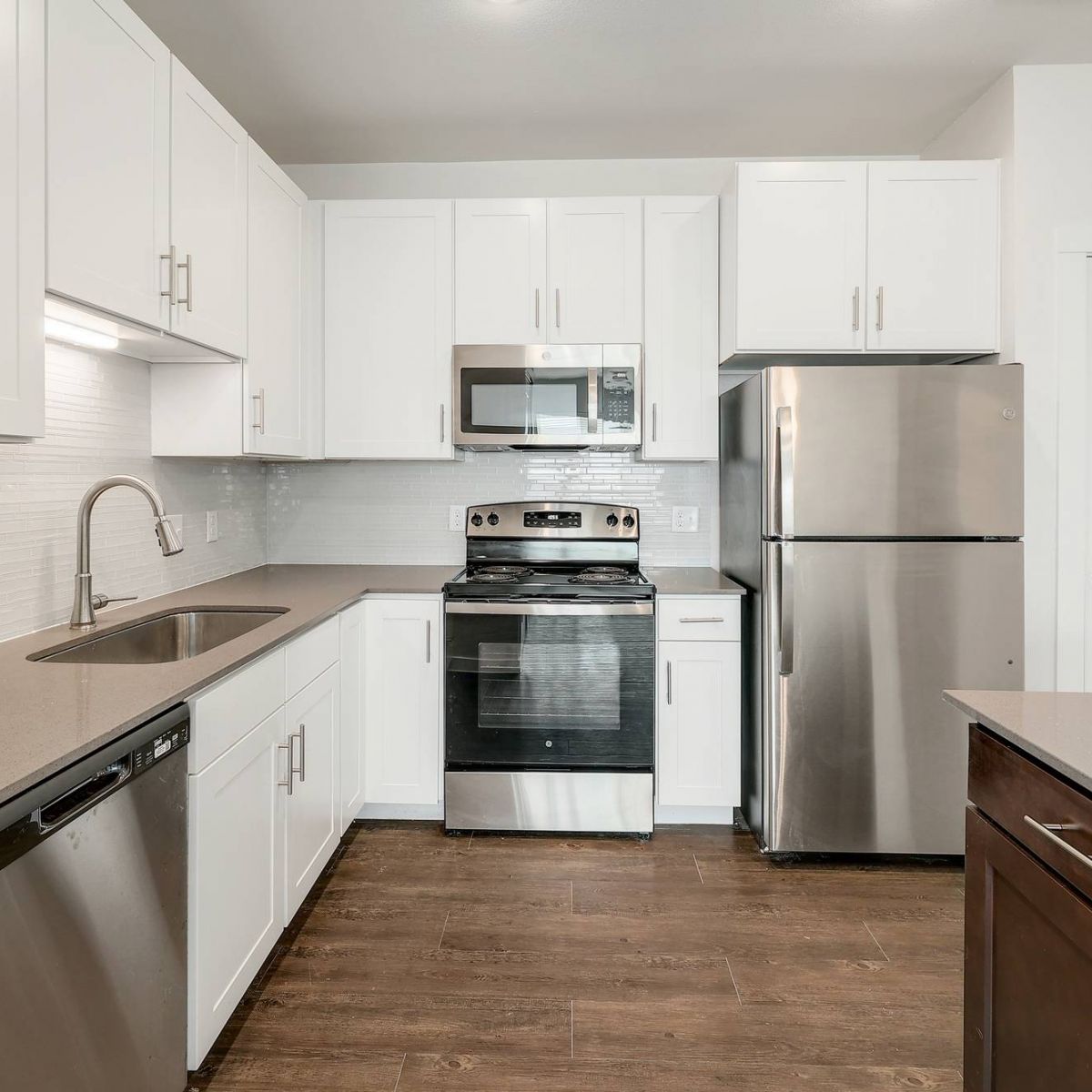 The Narrows Modern kitchen with white cabinets, stainless steel appliances, and brown wood flooring.