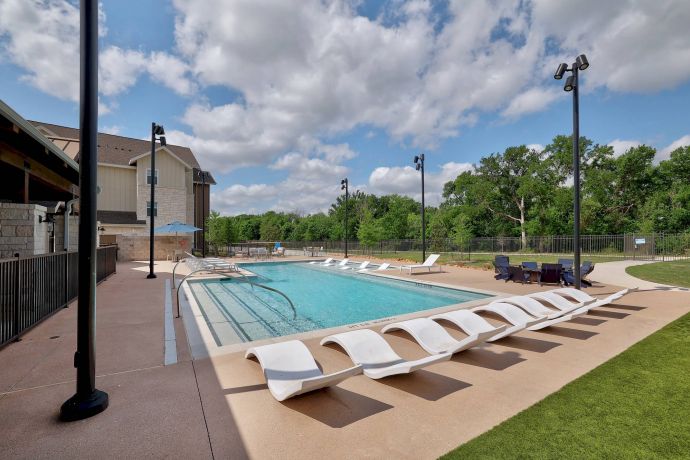 The Narrows Outdoor pool with white lounge chairs, surrounded by trees and a building under a partly cloudy sky.