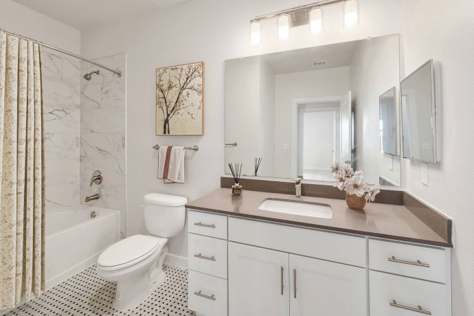 The Narrows Modern bathroom with white cabinets, a large mirror, a bathtub with a floral shower curtain, and wall art.