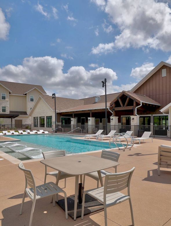 The Narrows Outdoor swimming pool with lounge chairs, patio tables, and modern buildings under a partly cloudy sky.