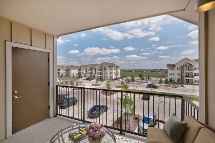 The Narrows Apartment balcony view overlooking a parking lot, grassy area, and several residential buildings under a blue sky.